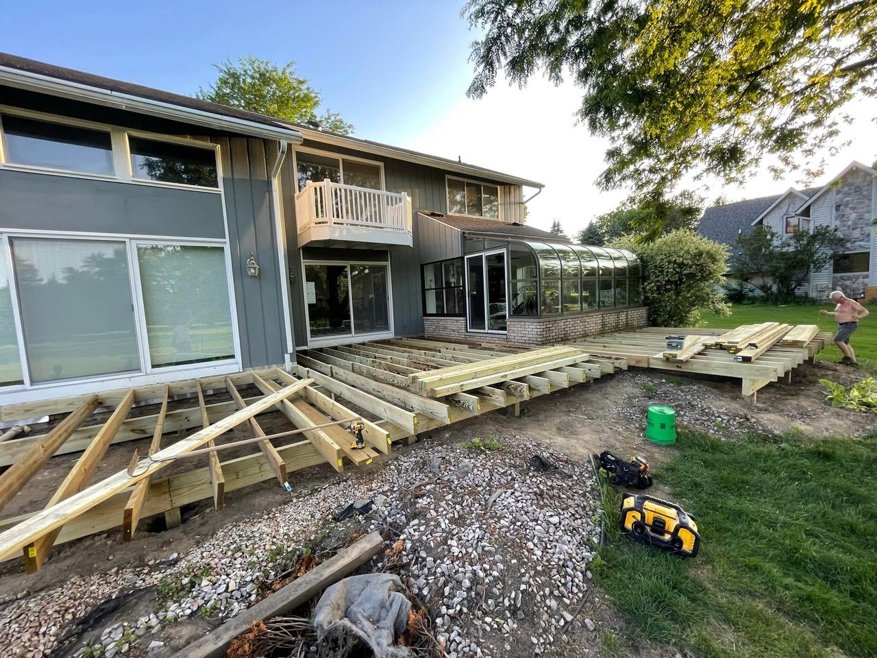 Deck joists framed on footings behind a house with a curved sunroom