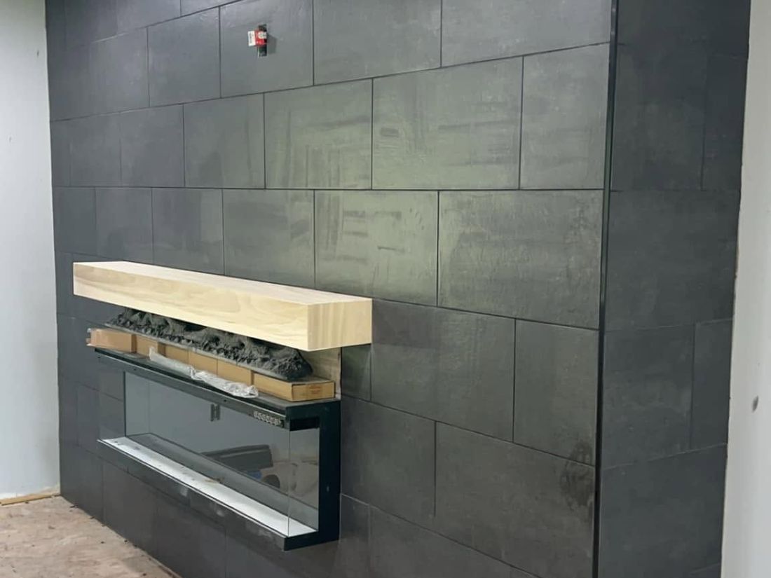 Large-format dark tile fireplace wall with a solid wood mantel and linear fireplace