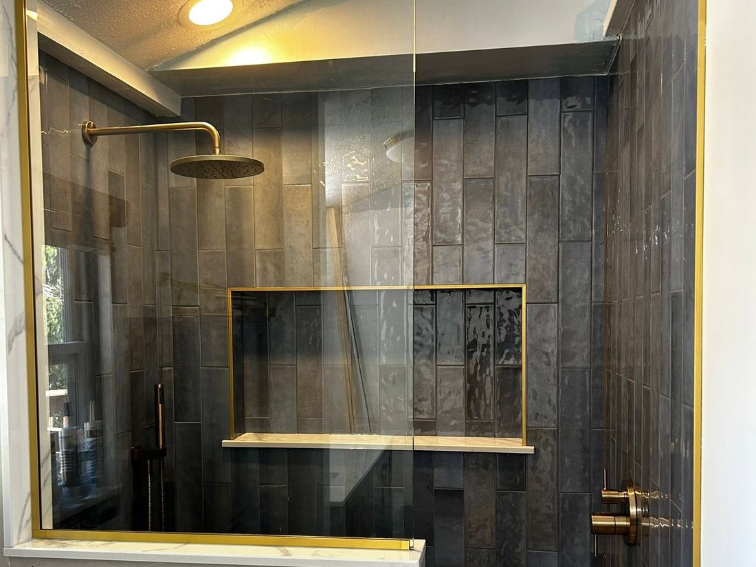 Vertical tile shower with a framed niche, stone shelf and brass fixtures