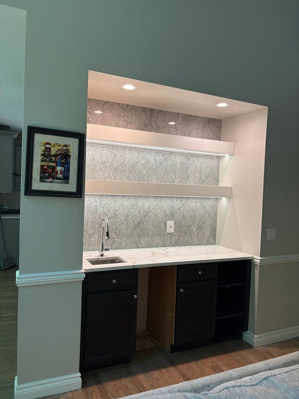 Wet bar after, with quartz counter, slab backsplash and lit floating shelves